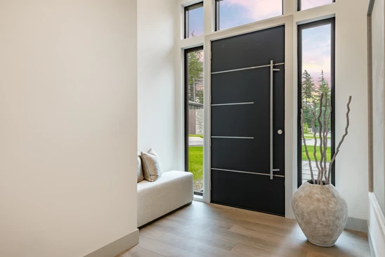 Entrée principale d'une maison résidentielle avec double porte en bois brun à panneaux surélevés, encadrée par des colonnes blanches cannelées sur bases en pierre naturelle multicolore
