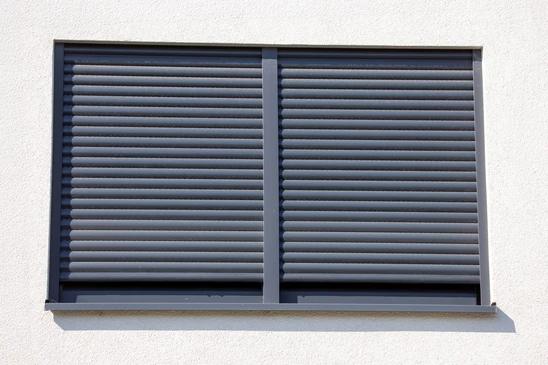 Façade extérieure de bâtiment résidentiel en briques oranges avec fenêtre équipée d'un volet roulant blanc partiellement ouvert