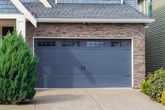 Garage résidentiel avec porte sectionnelle blanche partiellement ouverte, façade en bardage bois peint beige, toiture à pignon avec bardeaux d'asphalte