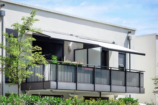 Balcon moderne d'appartement avec jardinières suspendues noires contenant plantes vertes et fleurs colorées